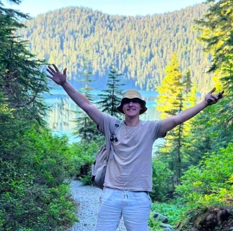 Pijus smiling on a forest trail beside a mountain lake
